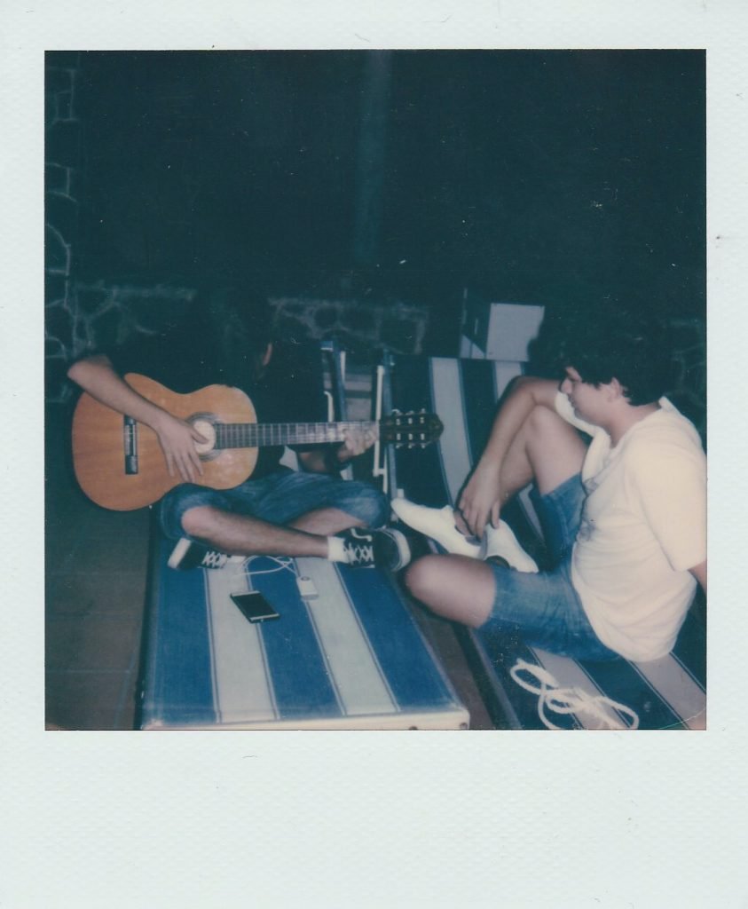 two men sitting while one is playing the guitar and the other is listening
